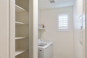 A laundry room with a washing machine, a dryer, and a shelf with laundry supplies.
