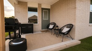 Zona exterior coberta amb una barbacoa, un armari negre, dues cadires negres i un felpudet.