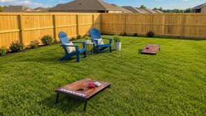 A backyard with a wooden fence, two blue Adirondack chairs, a small table, and a wooden board game.