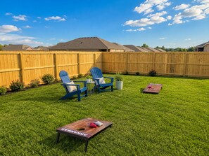 Un jardin avec une clôture en bois, deux chaises Adirondack bleues, une petite table et un jeu de société en bois.