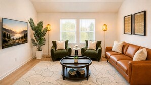 A living room with a sofa, two armchairs, a coffee table, a potted plant, and a painting on the wall.