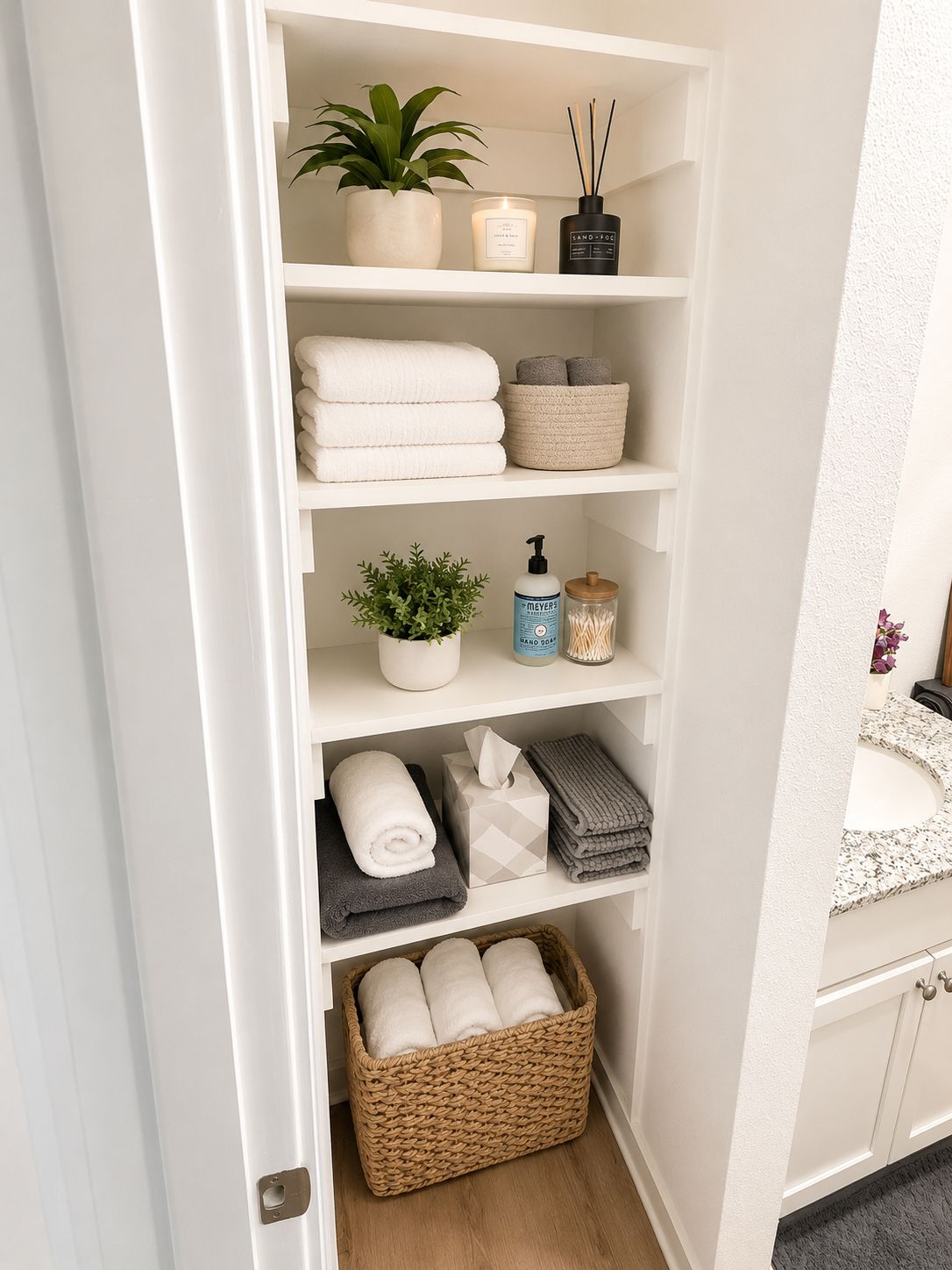 Une salle de bain bien rangée, avec un meuble-lavabo blanc, une étagère contenant des articles de toilette et un panier rempli de serviettes.