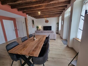 A dining area with a wooden table and chairs, a sofa, a television, and a stone wall. - Léontine's Oustalou (Ladinhac)