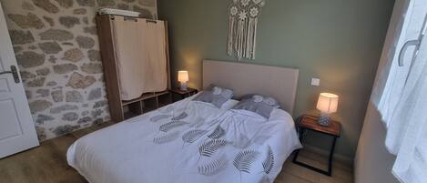 Un dormitorio con una cama, dos mesitas de noche con lámparas, un atrapasueños colgado en la pared y una pared con diseño de piedra.