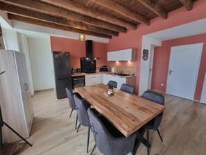 A modern kitchen with a wooden table and chairs, a refrigerator, and a microwave. - Léontine's Oustalou (Ladinhac)
