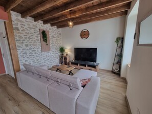 Una sala de estar con un sofá, un televisor, una mesa de centro de madera y una pared de piedra.