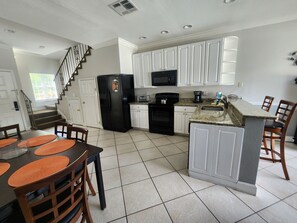 A modern kitchen with white cabinets, a black refrigerator, a microwave, and a stove. There is a dining area with a table and chairs. - BBQ Grills, Free Shuttle to Disney and more  # 5 (Orlando)