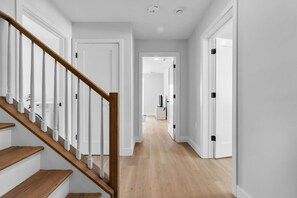 A clean, modern hallway with a wooden staircase, white walls, and a light wooden floor.