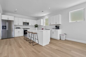 A modern kitchen with white cabinetry, a stainless steel refrigerator, a microwave, and a coffee maker.
