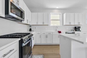 A modern kitchen with white cabinets, a stove, a microwave, and a coffee maker. - Luxury Ocean-Block Penthouse, Ocean Views (Seaside Heights)