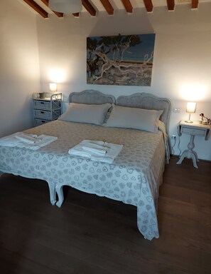 A bedroom with a bed, two bedside tables, a nightstand, a lamp, a painting, and a wall-mounted light fixture. - FARMHOUSE WITH OCEAN VIEW (Toscana)