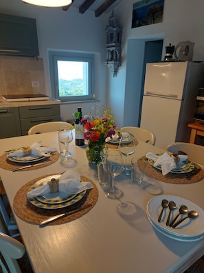 A dining area with a table set for four, a refrigerator, a window, and a kitchen area with cabinets and a microwave. - FARMHOUSE WITH OCEAN VIEW (Toscana)