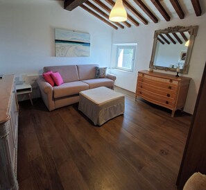 Una sala de estar con sofá, reposapiés, cómoda de madera y un cuadro en la pared.