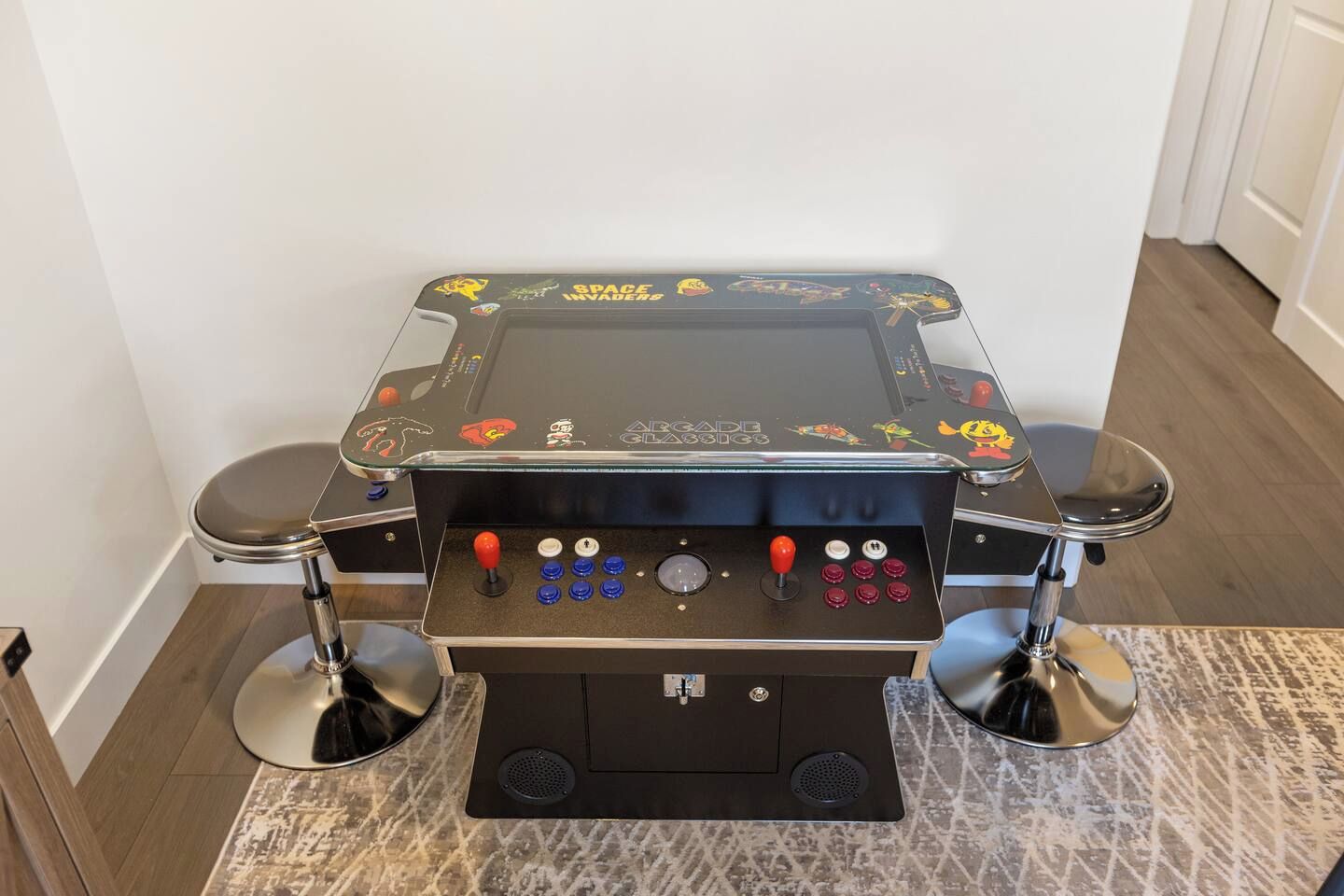 Een tafelvoetbaltafel met een zwart speeloppervlak en kleurrijke figuurstickers, twee metalen poten en een bedieningspaneel met knoppen en joysticks.