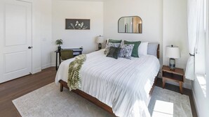 Ein Schlafzimmer mit Bett, Schreibtisch, Stuhl, Nachttisch mit Lampe, Spiegel und Tür.