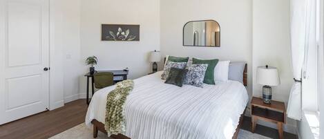 Une chambre à coucher comprenant un lit, un bureau, une chaise, une table de chevet avec une lampe, un miroir et une porte.