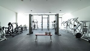 Ein Fitnessstudio mit verschiedenen Trainingsgeräten, darunter eine Bank, Gewichtsständer und Cardiogeräte.