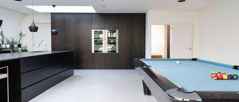 A modern pool room with a pool table, dark cabinetry, and a skylight.