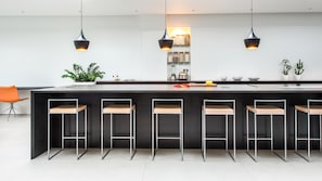 Een moderne keuken met een centraal eiland, barkrukken, hanglampen en een potplant.
