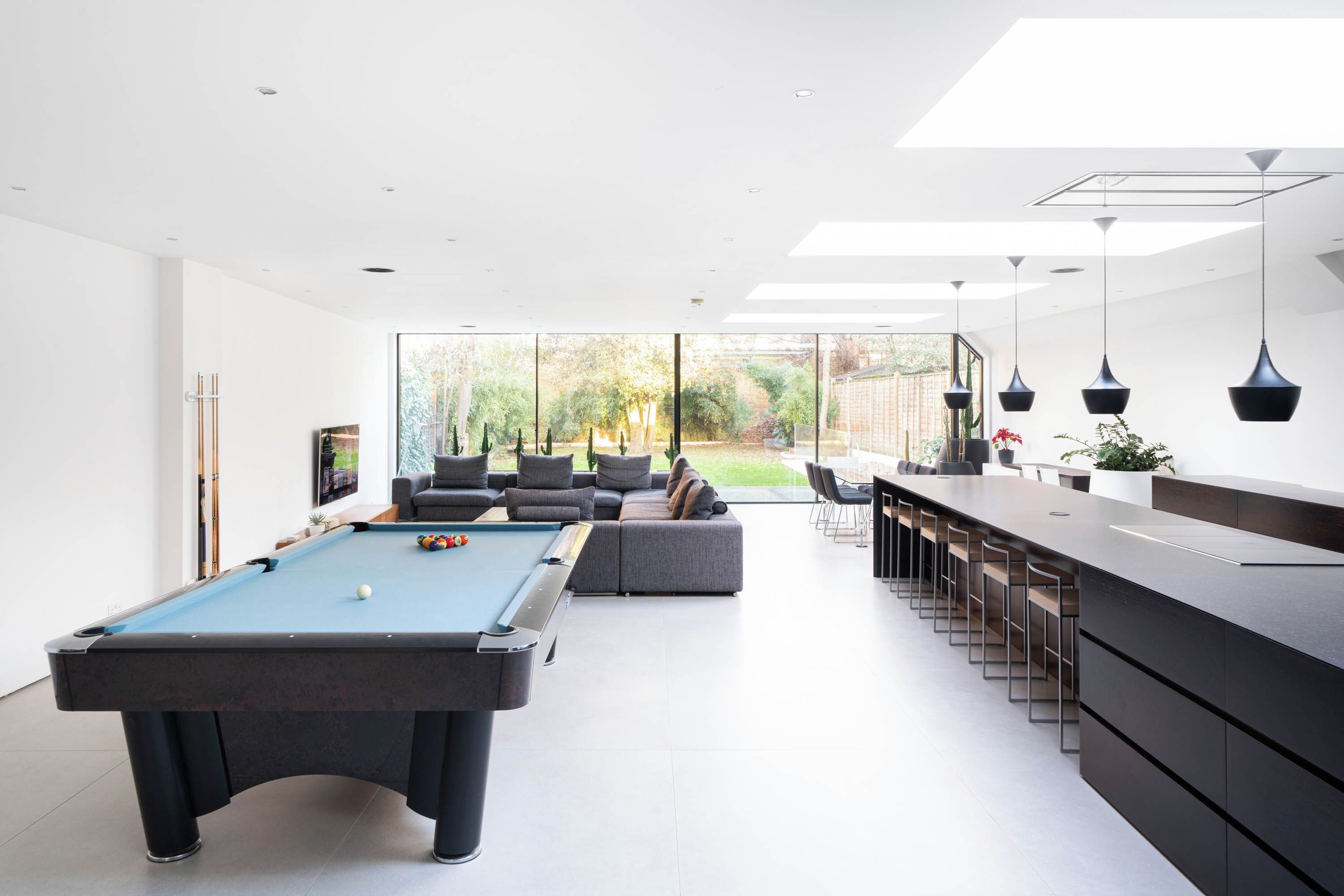 A modern living room with a pool table, a bar area, and a large window offering a view of the outdoors.