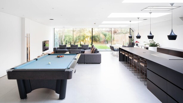 Una sala de estar moderna con mesa de billar, zona de bar y un amplio ventanal con vistas al exterior.