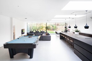 Ein modernes Wohnzimmer mit Billardtisch, Bar und großem Fenster mit Blick ins Freie.