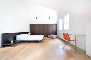 Een moderne slaapkamer met een bed, een kleine plant, een stoel en een raam.