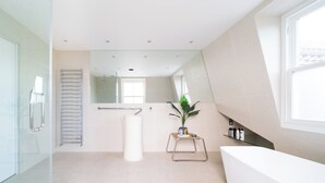 Un baño moderno con una bañera grande, cabina de ducha de vidrio, perchero, espejo y una planta en maceta.