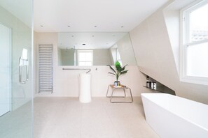 Une salle de bain moderne avec une grande baignoire, une cabine de douche en verre, un porte-serviettes, un miroir et une plante en pot.