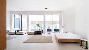 Un dormitorio moderno con una cama grande, un área de descanso con sofás y vistas al exterior a través de amplios ventanales.