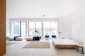 Une chambre moderne dotée d’un grand lit, d’un coin salon avec des canapés et offrant une vue sur l’extérieur grâce à de grandes fenêtres.