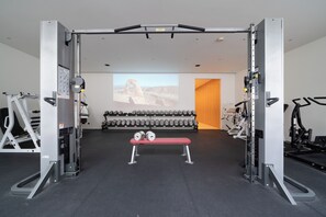 Ein Fitnessraum mit Gewichteinrichtung, einer Hantelbank und einem an der Wand befestigten Bildschirm, der ein Bild zeigt.