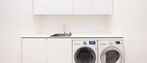 A compact laundry area with two front-loading washing machines and a sink.