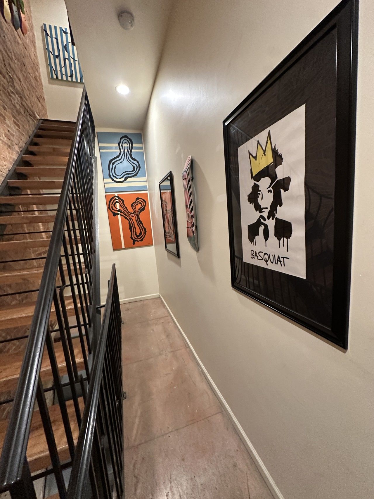 Un pasillo con una escalera, una pared con arte abstracto y un cuadro con una corona y la palabra 'BASQUIAT'.