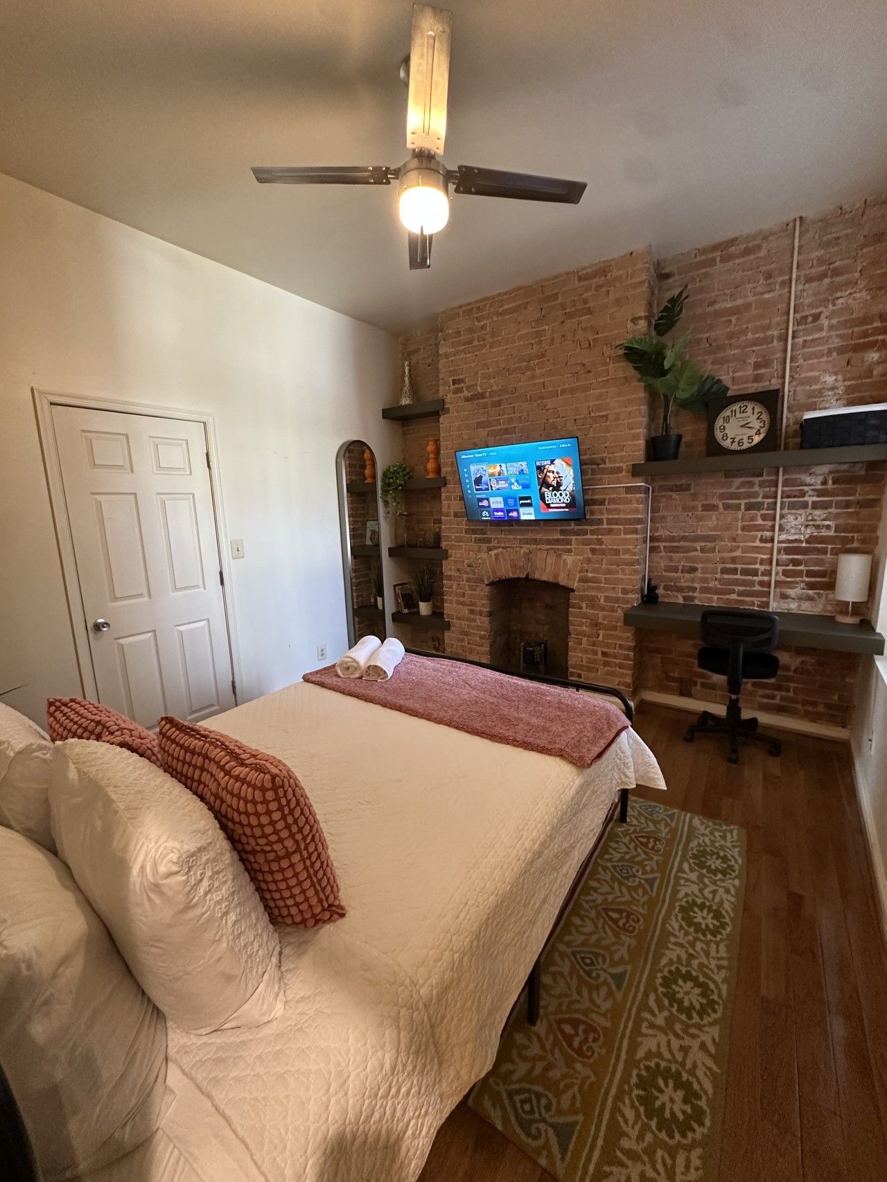 Een slaapkamer met een bed, een plafondventilator, een bakstenen muur, een wandtelevisie en een open haard.