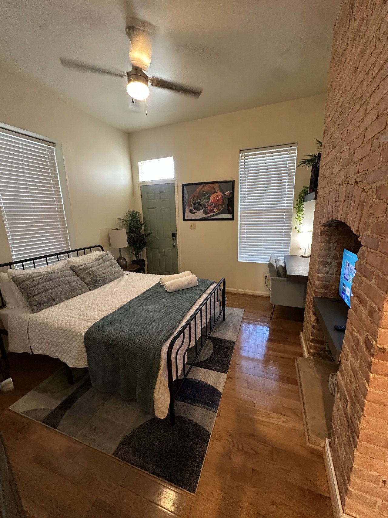 A bedroom with a bed, a ceiling fan, a fireplace, and a window with blinds.