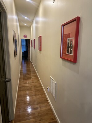 A hallway with wooden flooring, framed pictures on the walls, and a door on the left. - Eclectic Comfort: The Kitt – 2BR/2BA w/ Balcony Near MICA & JHU (Baltimore)