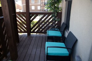 Eine Holzdar Terrasse mit zwei Stühlen und einem Tisch, einem Hollergeländer und Blick auf Gebäude im Hintergrund.