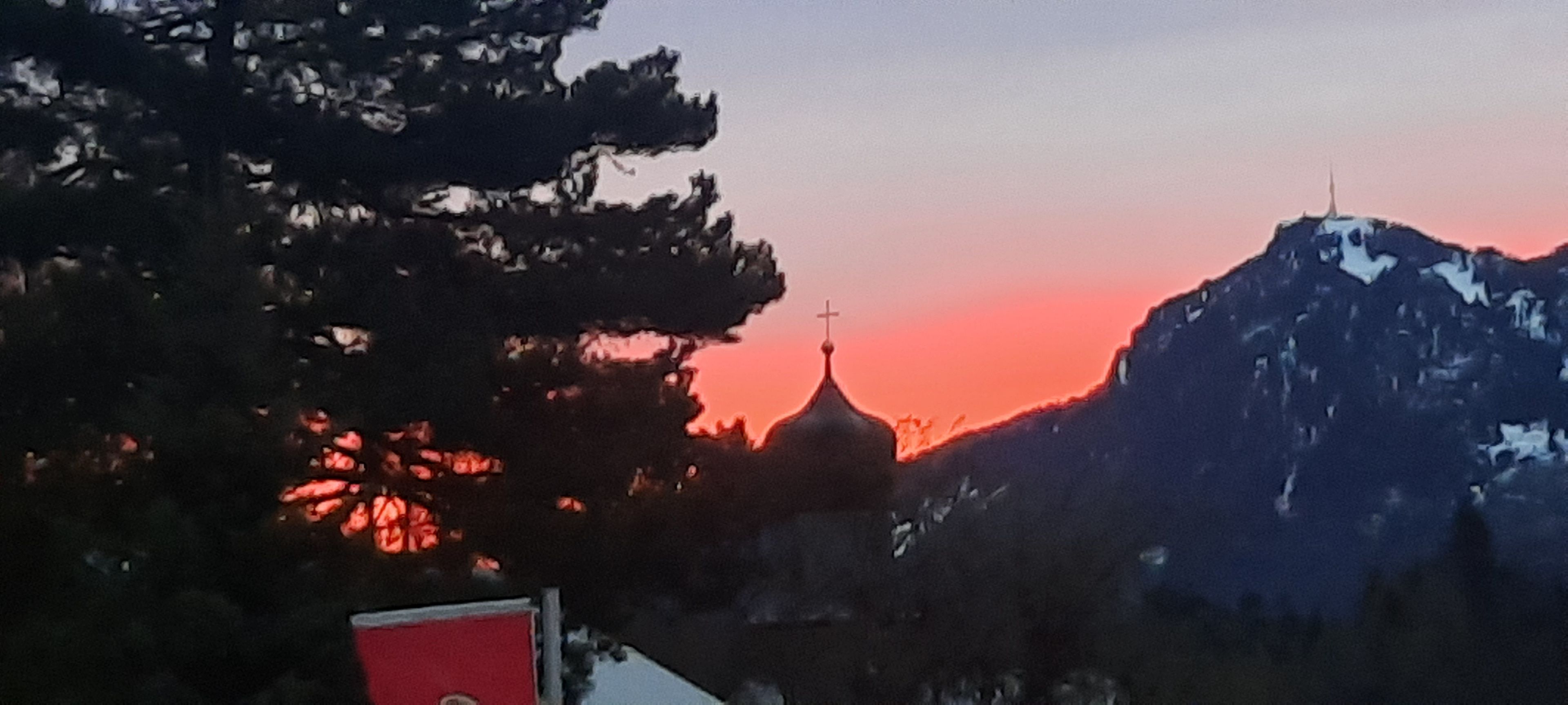 Una montaña con una cruz en la cima, una iglesia con una cúpula y una señal roja al frente.