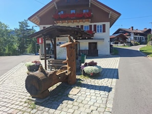 A wooden log structure with a sign, a building with a balcony, and flower beds in front.