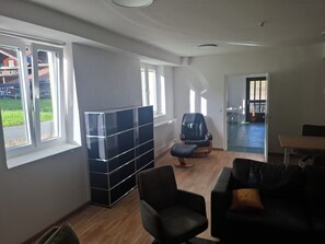 A spacious room with a large window, a black leather sofa, a black office chair, and a black storage unit.