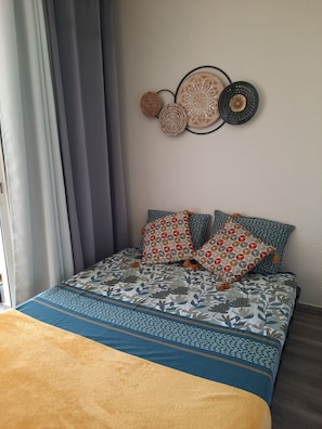 Cama com roupa de cama e almofadas estampadas, parede decorada com arte e janela com cortinas.