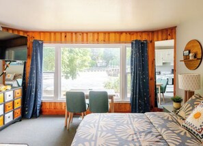 Un dormitorio con cama, escritorio, dos sillas, televisor y vistas a un espacio exterior.