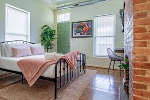A bedroom with a bed, a desk, a chair, a green door, and a wall-mounted picture. - Colorful & Quirky 1-BR Loft w/Private Deck | MICA, JH & UMMC (Baltimore)