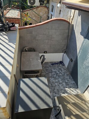 Ein kleiner Außenbereich mit Tisch und Stühlen, einem Fliesenboden und einer Steinmauer.