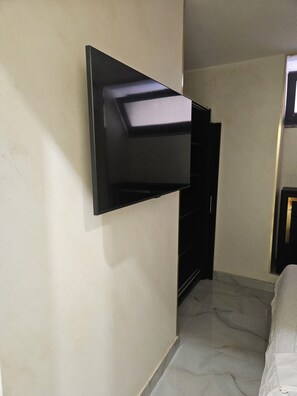 Ein Zimmer mit an der Wand montiertem Fernseher, einem Bett mit weißer Bettwäsche und einem Marmorboden.