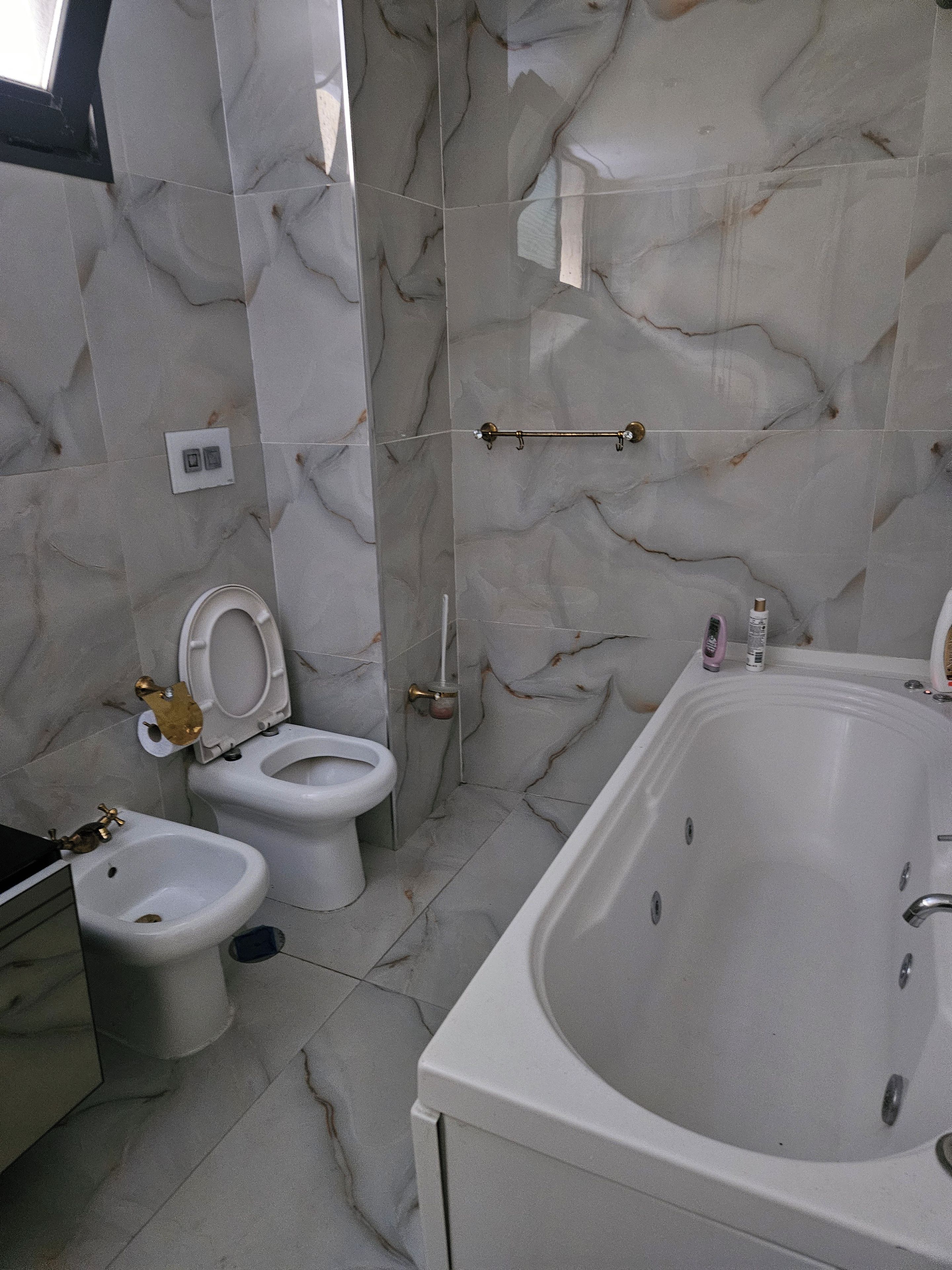 Um banheiro com banheira, dois vasos sanitários e um bidê.