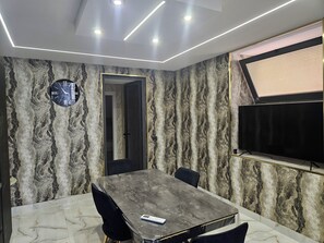 Ein Konferenzraum mit einer Wand im Marmor-Design, einer Uhr, einem Flachbildfernseher und einem digitalen Thermostat auf dem Tisch.