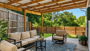 An outdoor patio with a wooden pergola, a beige sofa, a chair, and a small table. - Northgate: Closest Home to Aggieland! 3BR, 2.5BA (College Station)