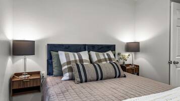 A neatly made bed with a quilted cover, two bedside tables with lamps, and a door to the right.